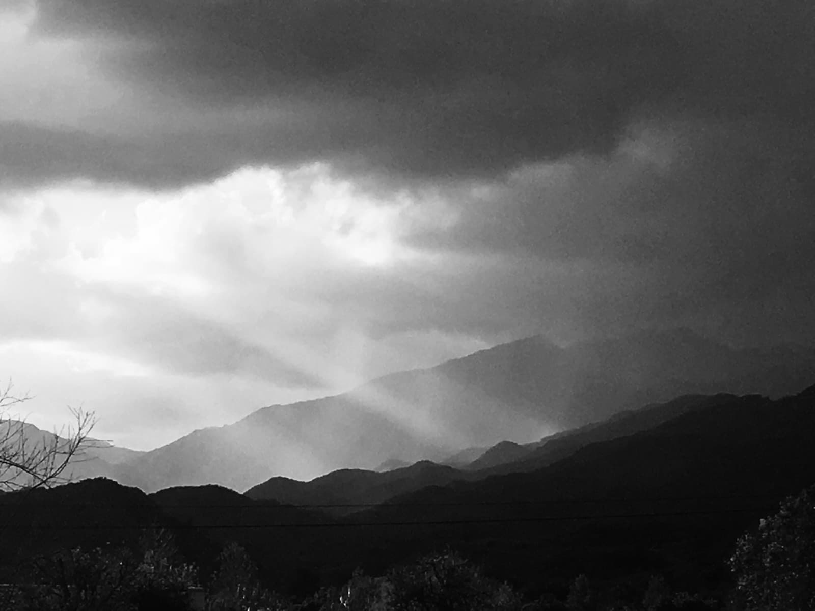 Sun breaking through cloud over a mountain range, black and white