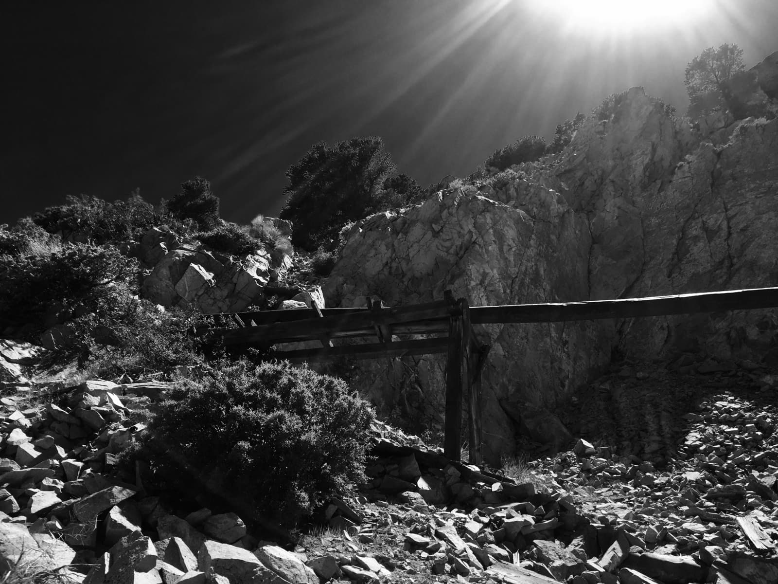 Sun flaring over a rocky slope and fence line, black and white