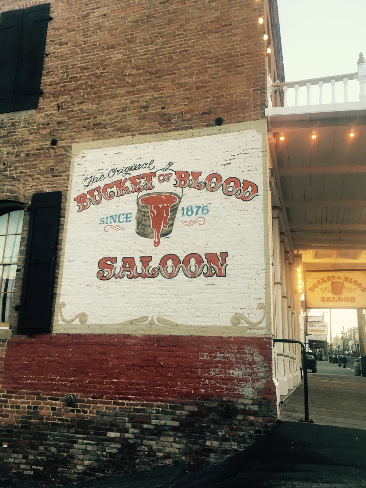 The painted brick wall sign of the Original Bucket of Blood Saloon, since 1876, beside a covered boardwalk