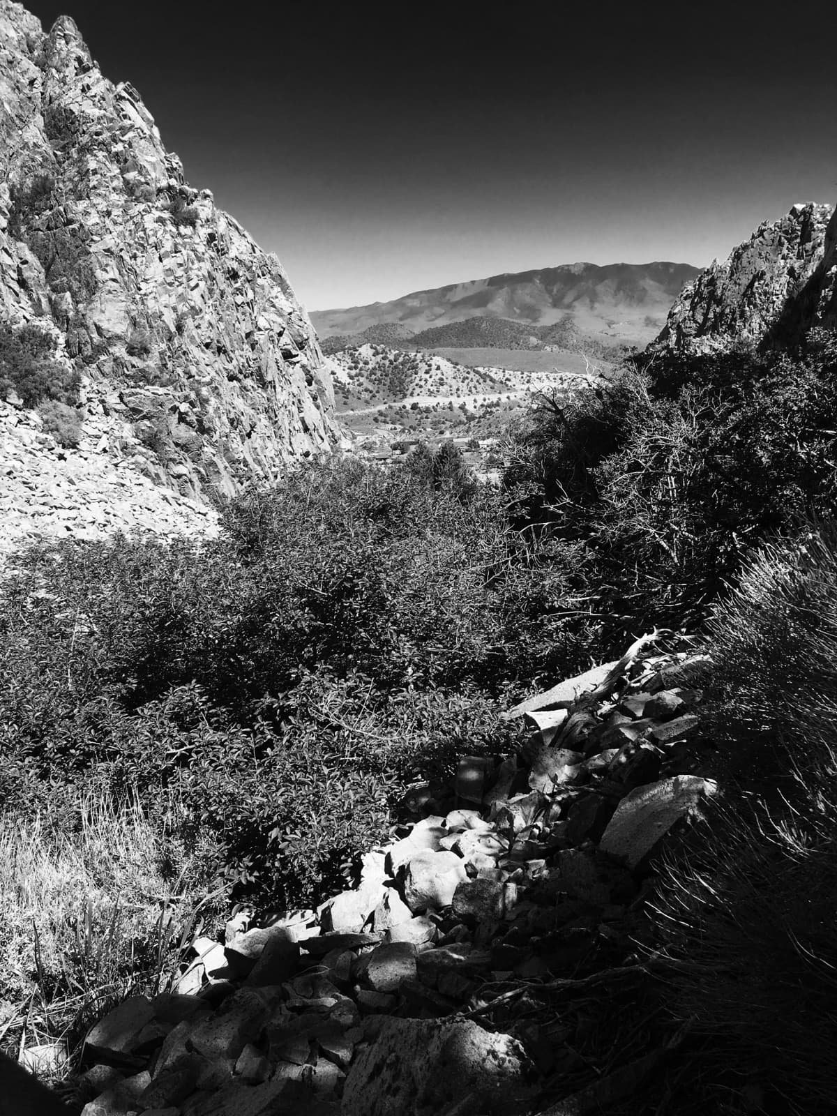 Black-and-white view through a rocky notch in the hills to a far valley and mountain