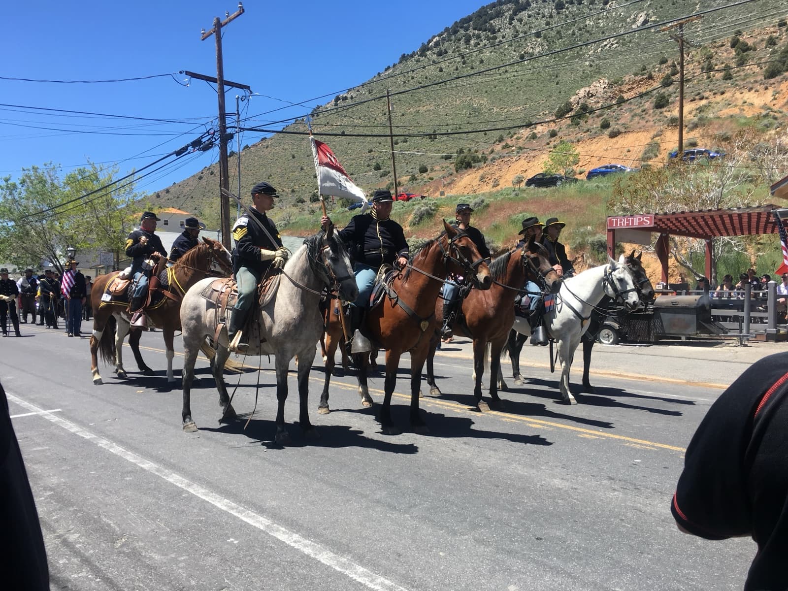 Riders in Civil War-era uniforms on horseback in a street parade, a dry hillside rising behind