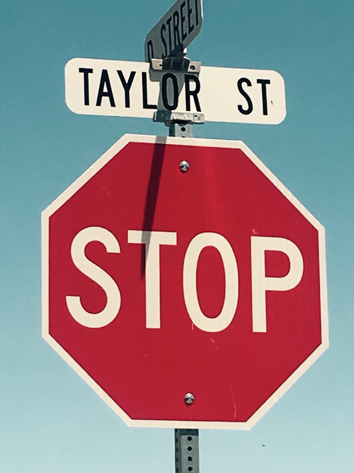 A red stop sign below a Taylor St street sign against a blue sky