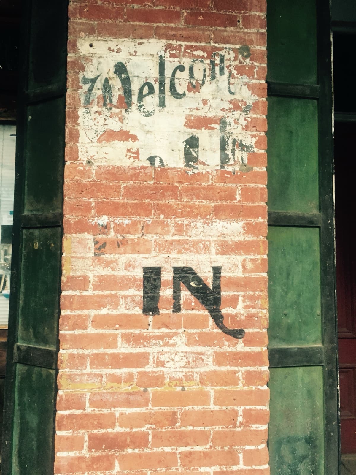 A faded painted sign reading Welcome on a red brick pillar, with the word IN below it